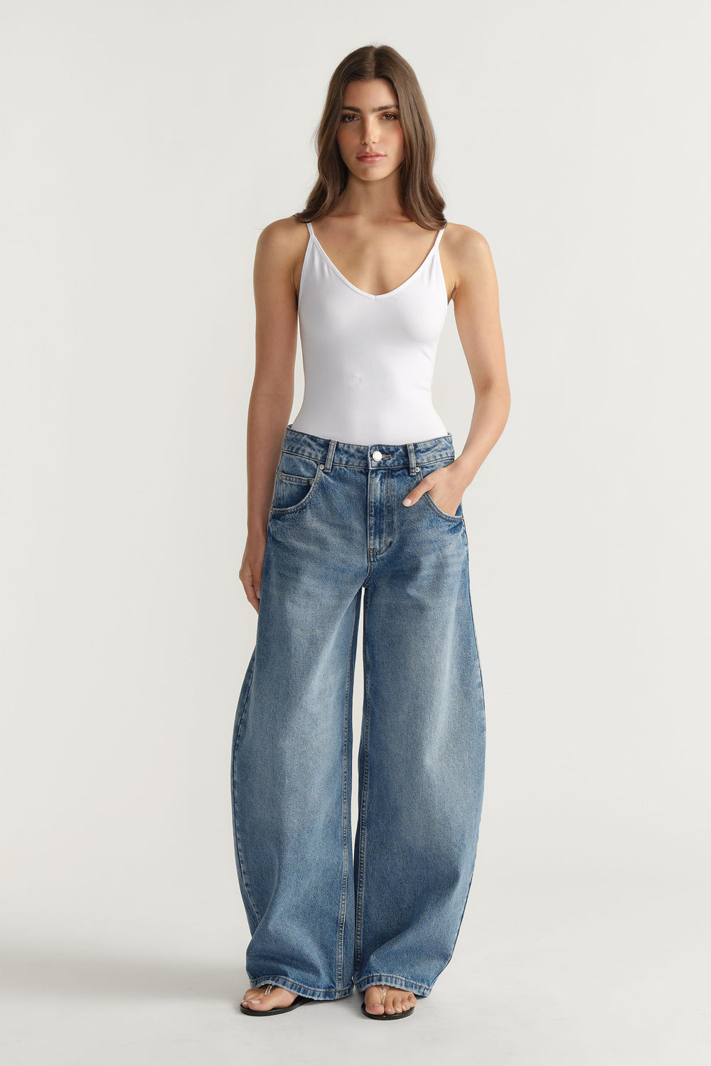 Front view of woman wearing relaxed wide-leg blue jeans paired with a fitted white thin strap tank top