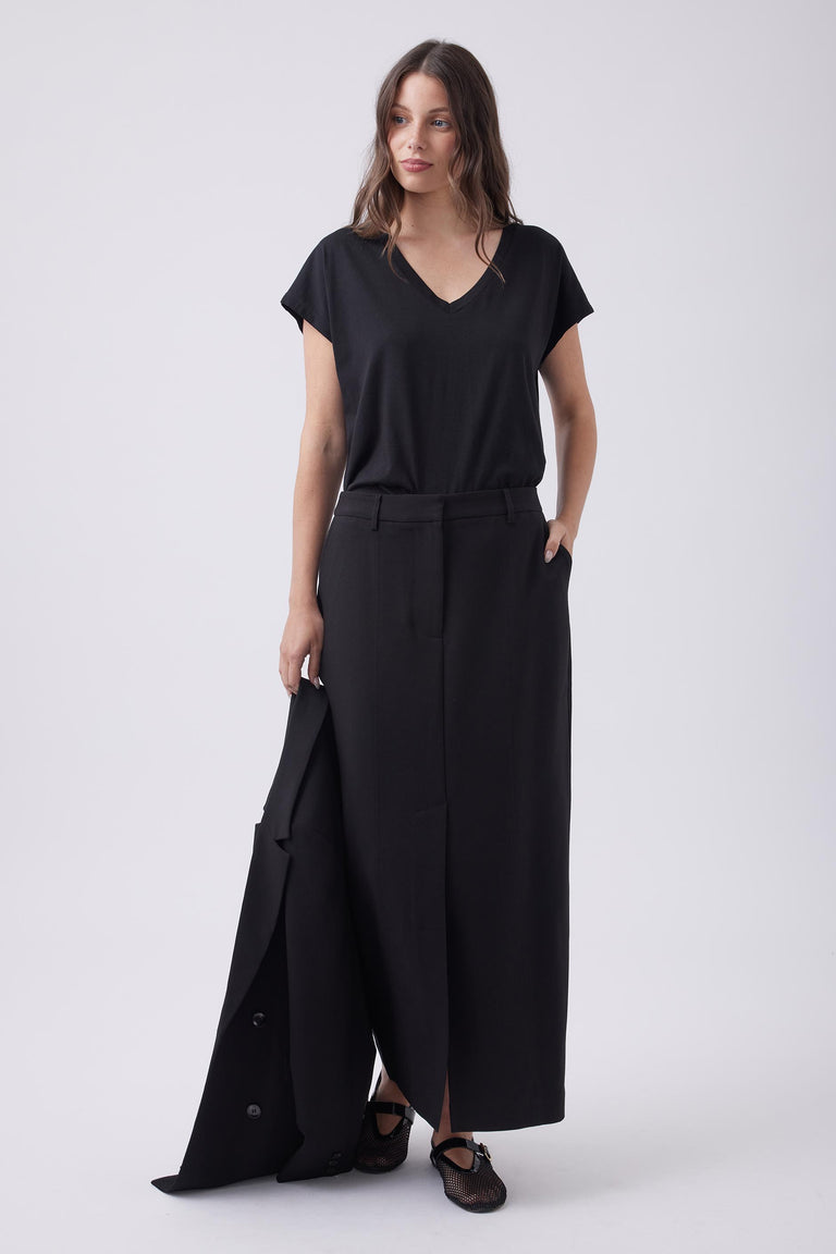 Woman wearing a black V-neck tee paired with a long black skirt, holding a matching blazer for a refined, modern look