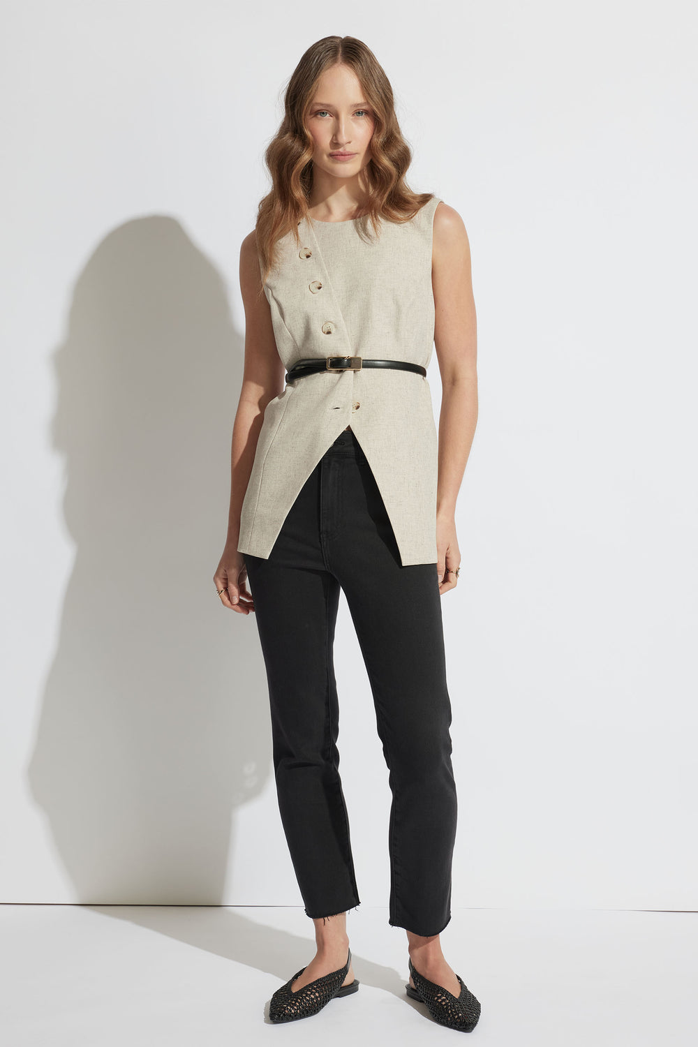 Portrait of a woman wearing black Becky Straight Leg Jean with raw hem, styled with a belted beige sleeveless top, gallery 1.