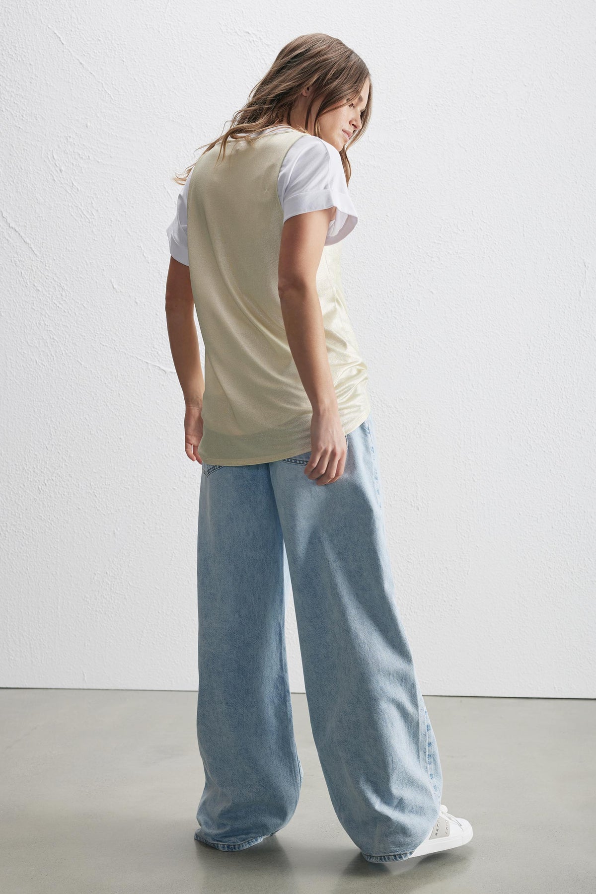Woman wearing a metallic sleeveless tank over a white tee with wide-leg jeans
