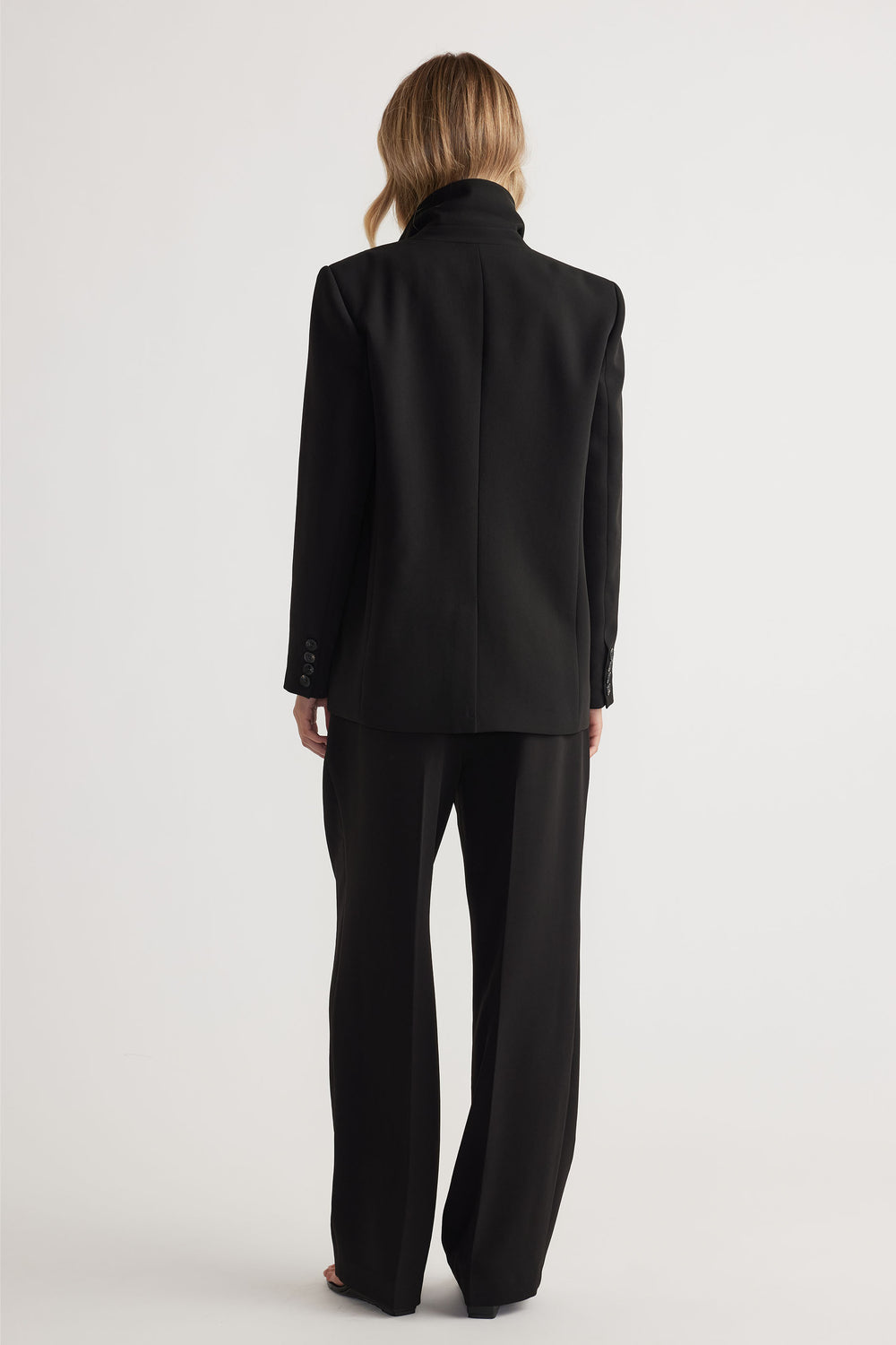 Back view of woman wearing black tailored pants with a matching blazer for a sleek, modern silhouette