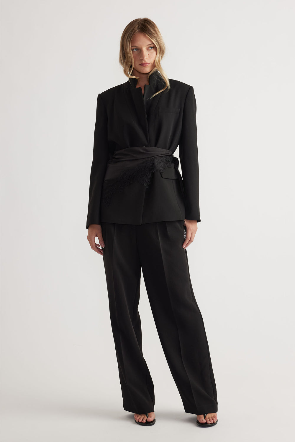 Woman wearing a structured black tailored blazer with matching wide-leg pants and a wrap belt detail at the waist