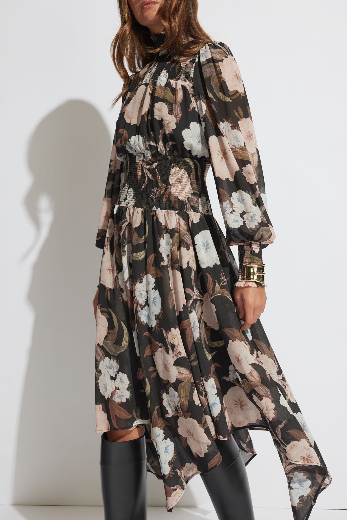 Woman wearing a long-sleeve shirred midi dress with a muted floral print paired with black boots and gold bracelets
