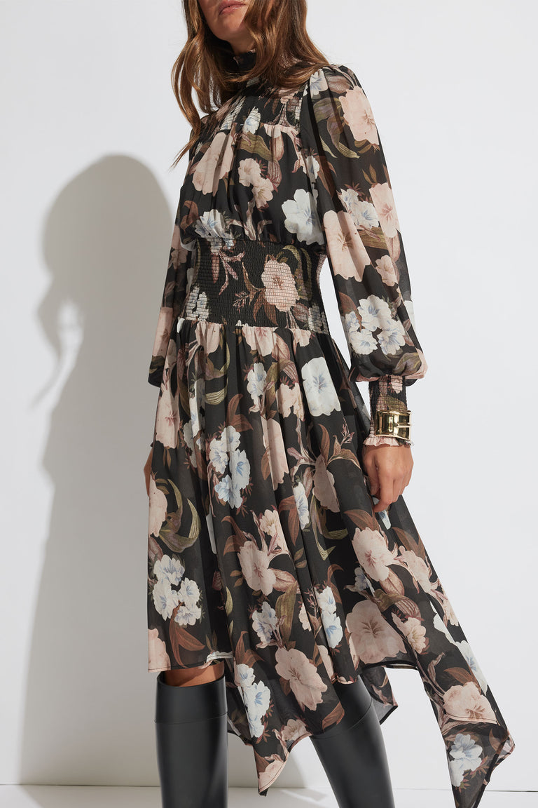 Woman wearing a long-sleeve shirred midi dress with a muted floral print paired with black boots and gold bracelets