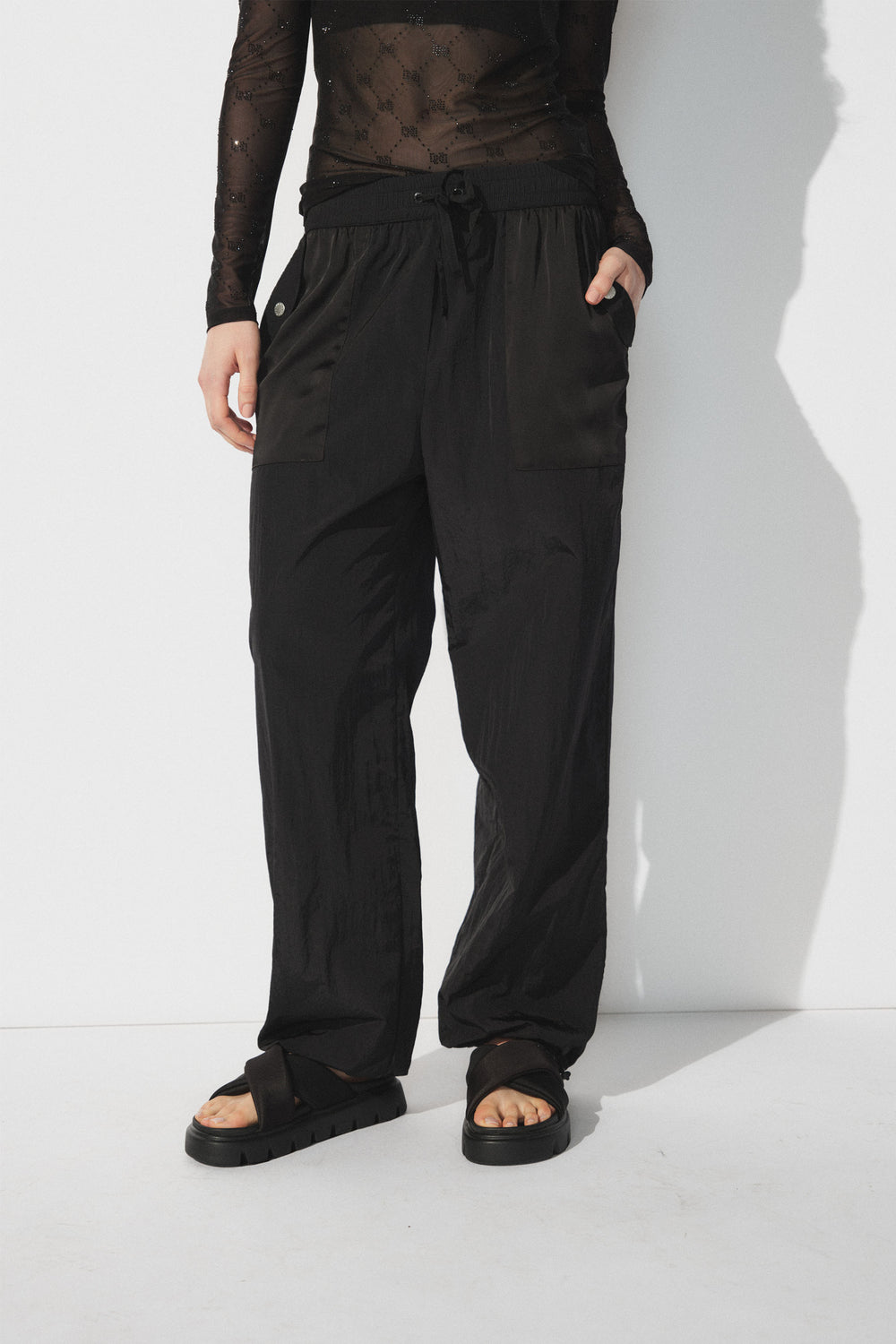 Woman wearing relaxed black parachute joggers with patch pockets and black platform sandals against a white backdrop