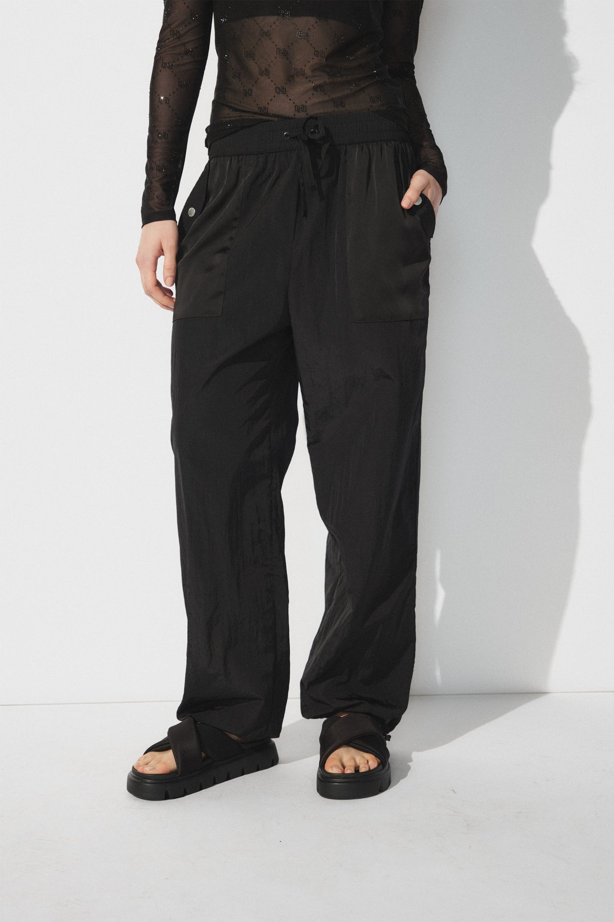 Woman wearing relaxed black parachute joggers with patch pockets and black platform sandals against a white backdrop