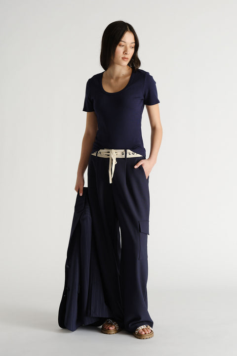 Woman wearing navy wide-leg pants with a white logo waistband, a fitted navy tee, and holding a matching jacket.