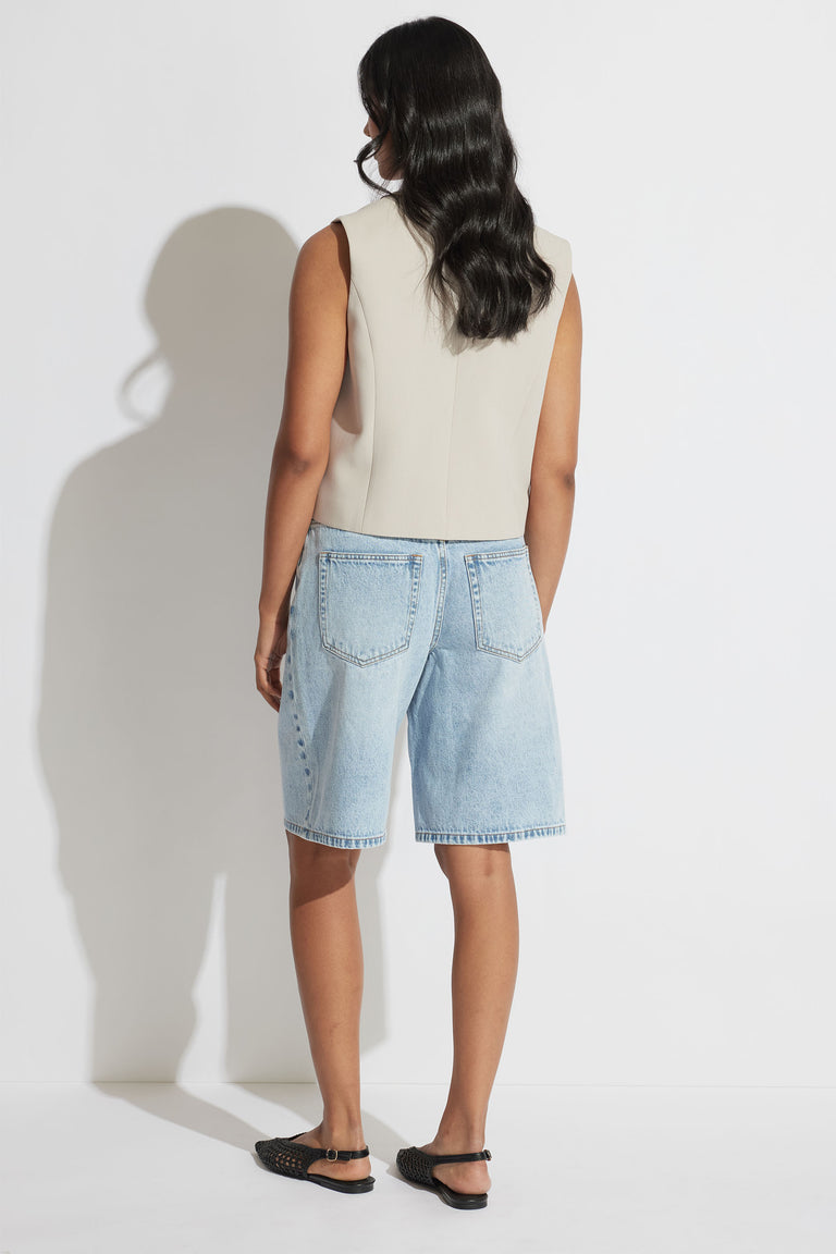 Woman wearing a sleeveless tailored vest in neutral tone paired with light wash denim shorts and black flats