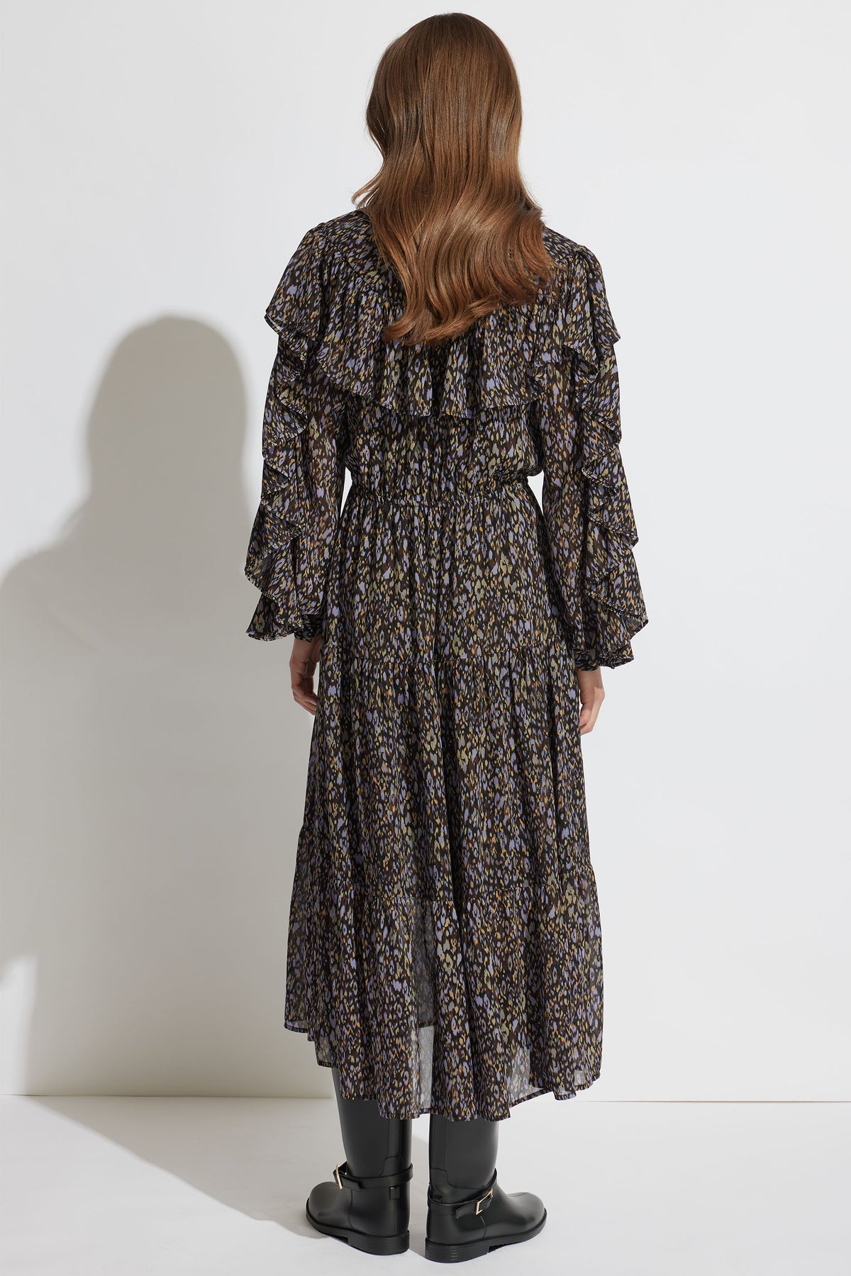 Back view of a woman wearing a dark floral midi dress with ruffles and long sleeves, paired with black boots.
