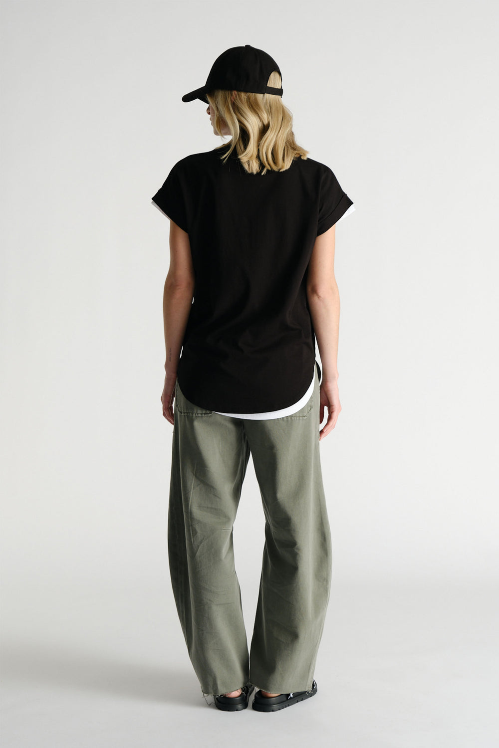 Rear view of woman wearing black D-Luxe Collegiate Tonal Tee with olive wide-leg pants and black cap by Decjuba Australian brand