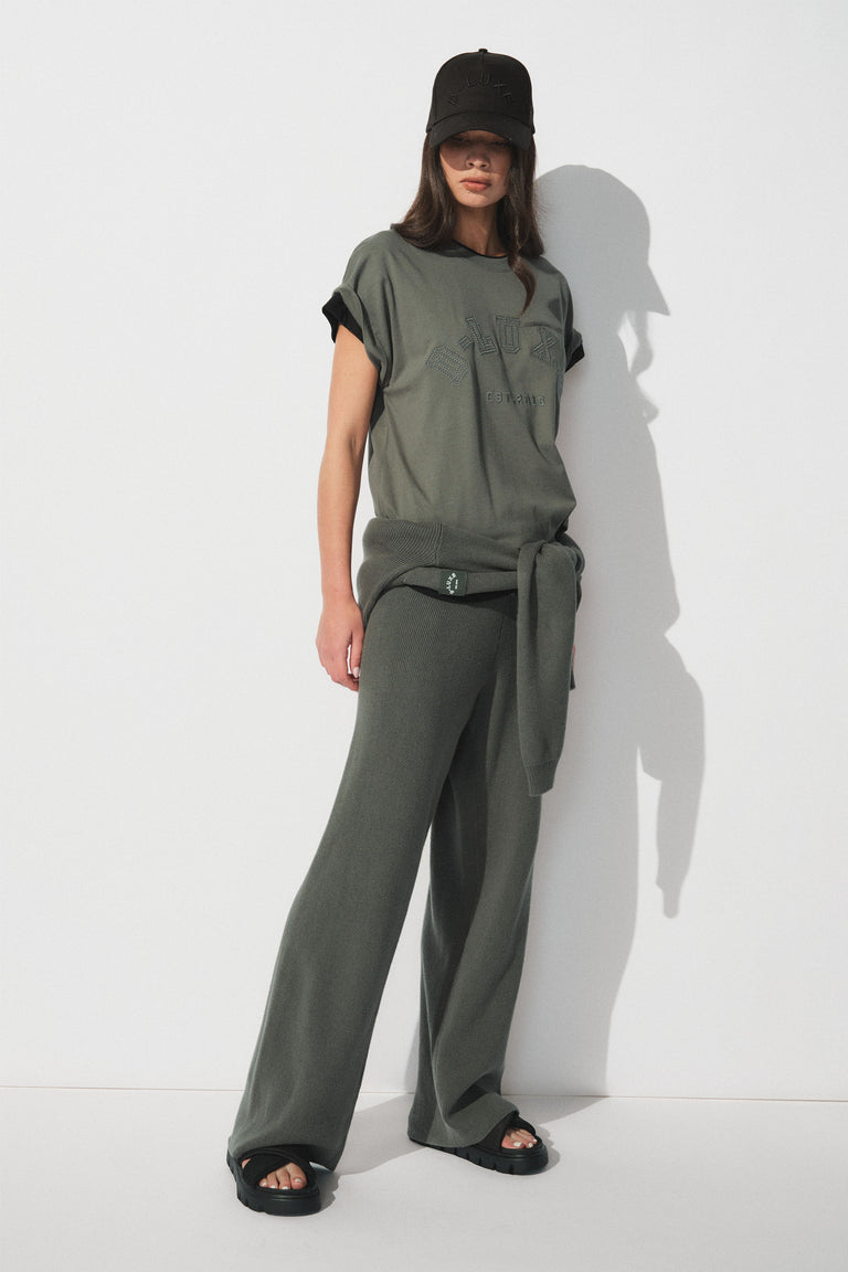 Woman wearing a dark green tonal tee with curved hem, wide leg pants, cap and black sandals