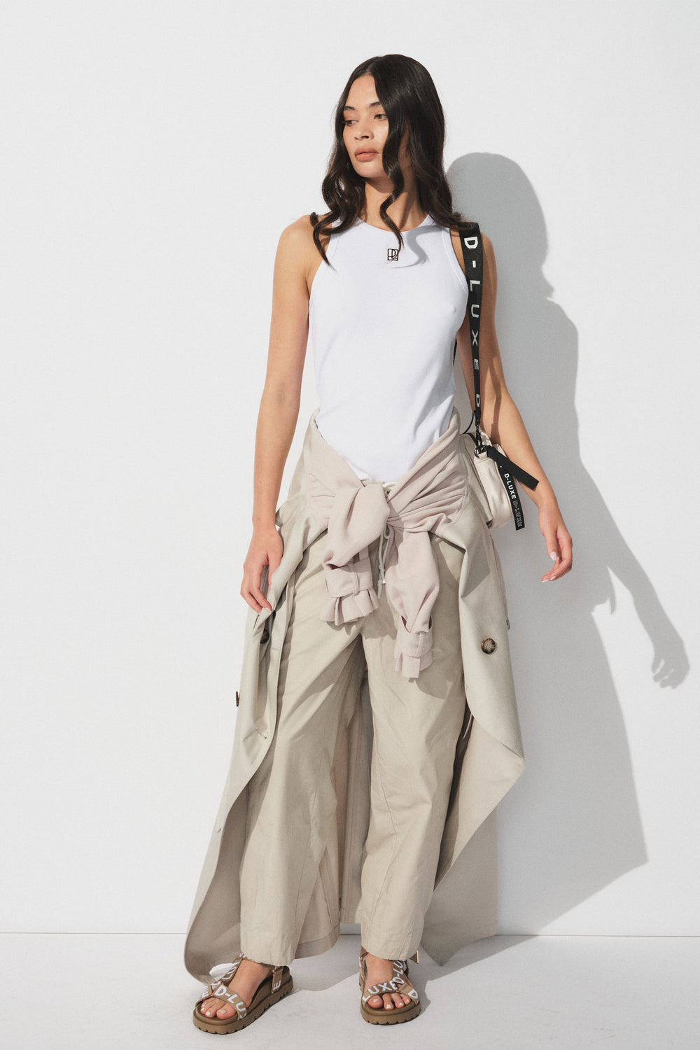 Woman wearing a white ribbed tank with wide beige pants and a beige jacket tied at the waist for a relaxed look