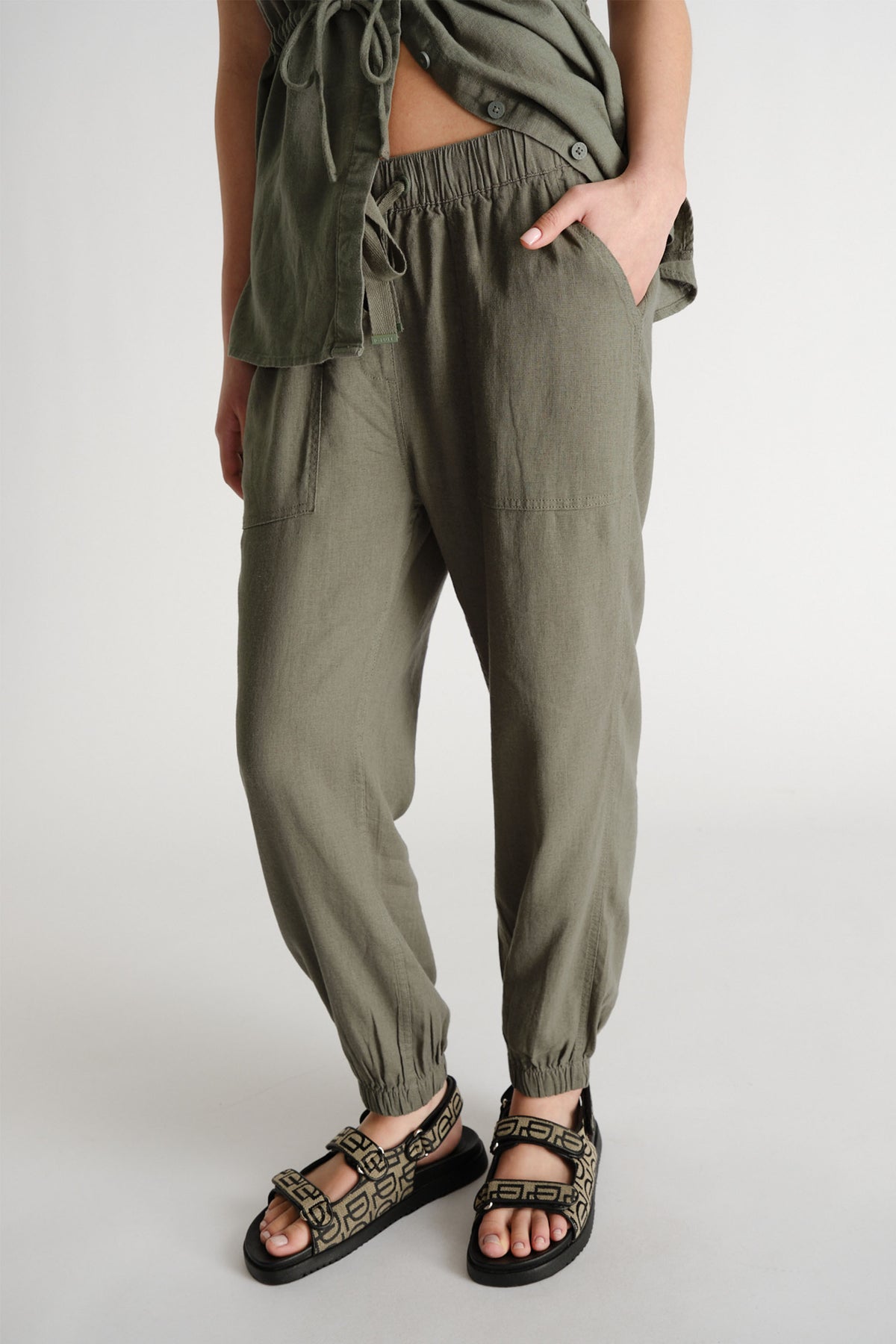 Olive green linen blend joggers with gathered ankles, worn with matching shirt and patterned sandals.
