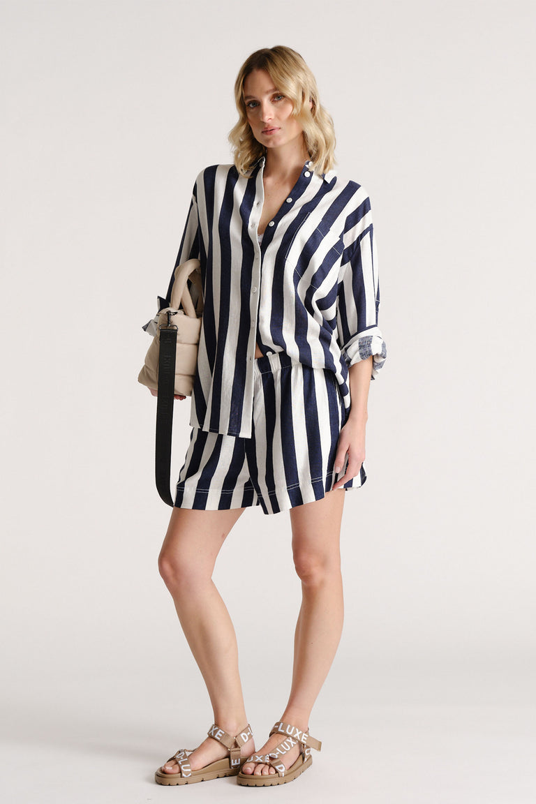 Woman wearing navy and white striped linen blend shorts with matching loose shirt and tan sandals, carrying a beige bag