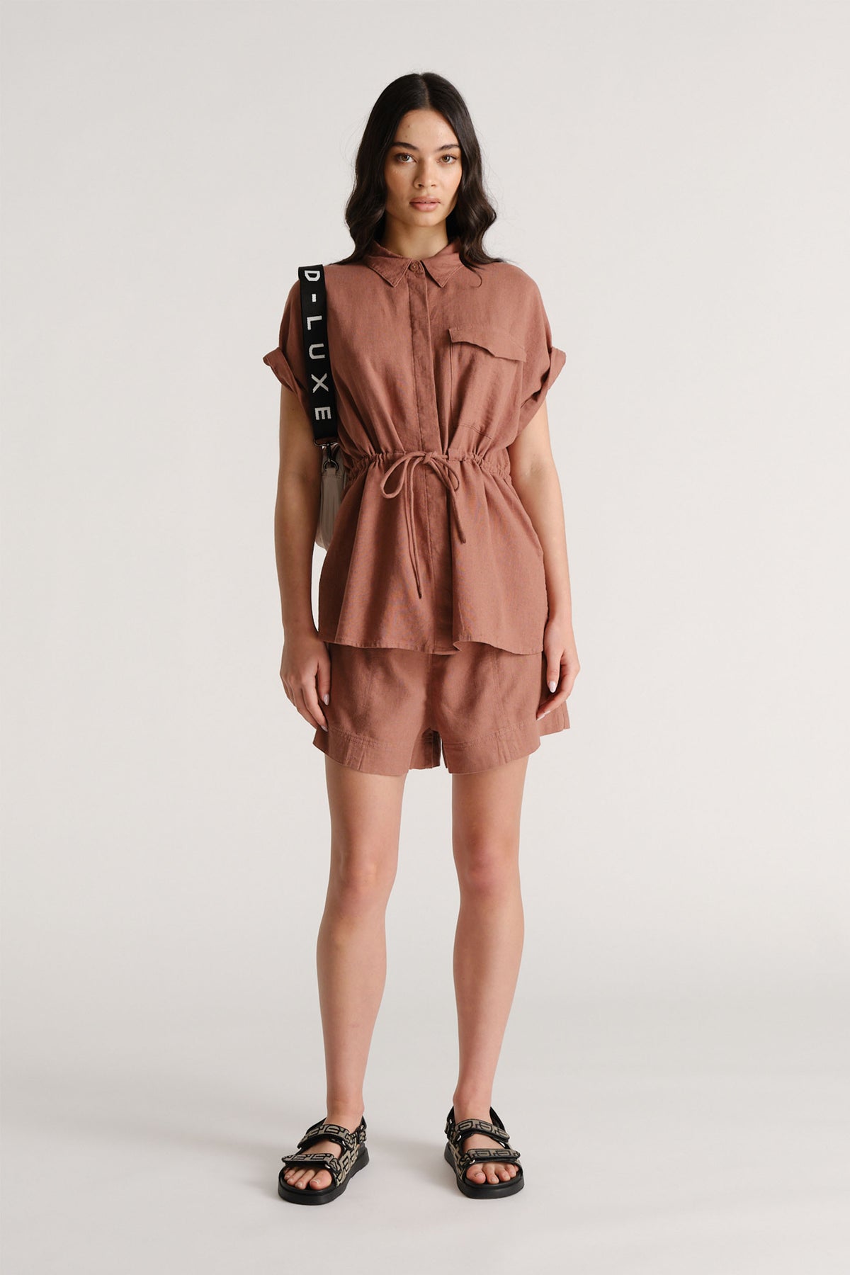 Woman wearing a rust linen shirt with drawstring waist and matching shorts with sandals