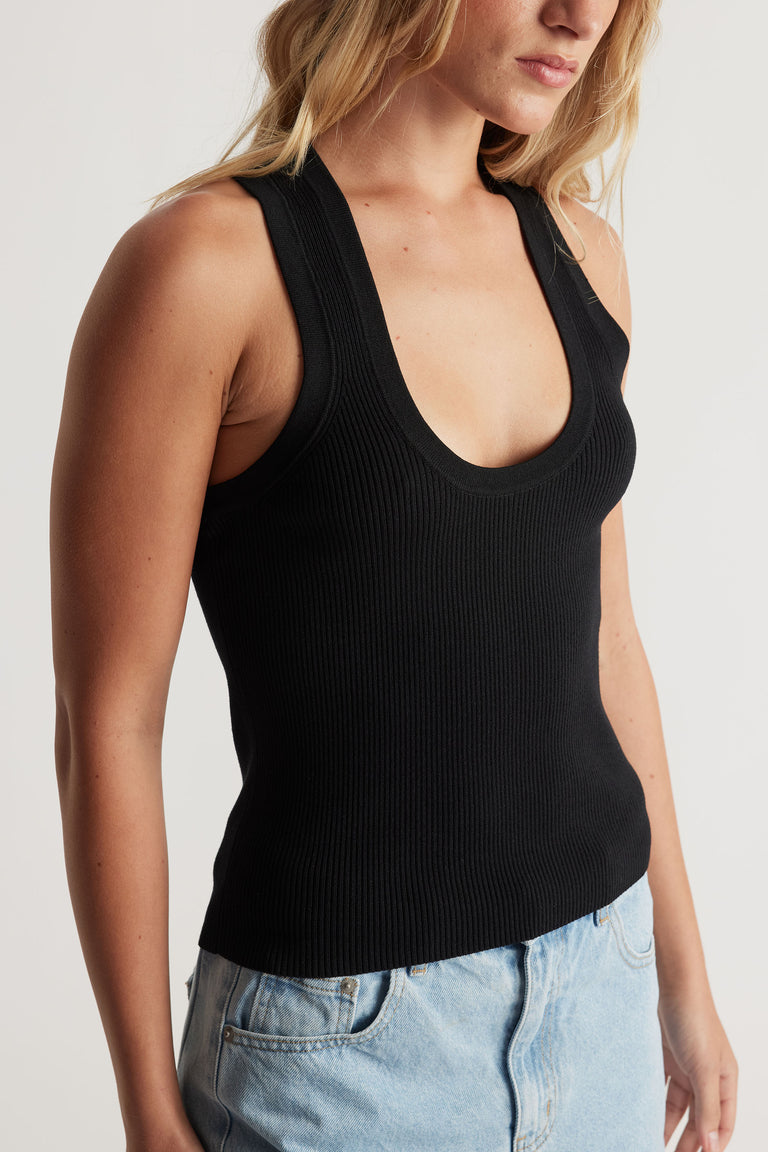 Close-up of a woman wearing a black ribbed knit tank with a scoop neckline paired with light-wash denim jeans.