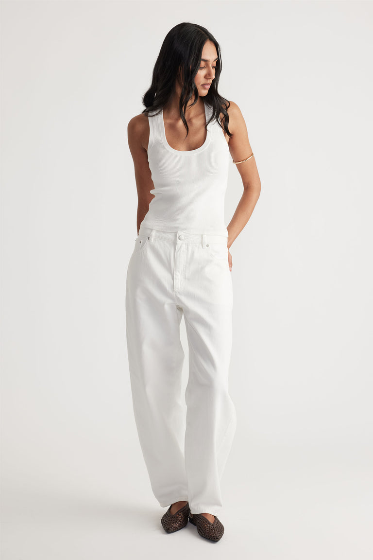 Woman wearing a fitted ivory knit tank top paired with relaxed white wide-leg jeans and dark woven flats