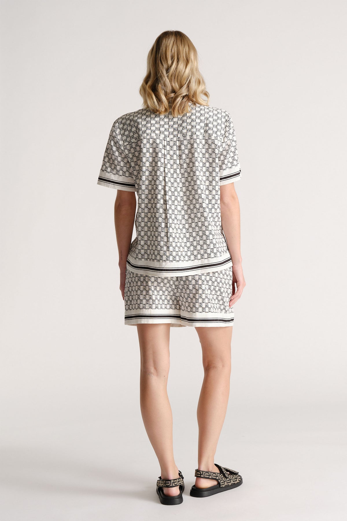 Woman wearing patterned short-sleeve top and matching shorts with striped trim, styled with patterned sandals, shown from behind.