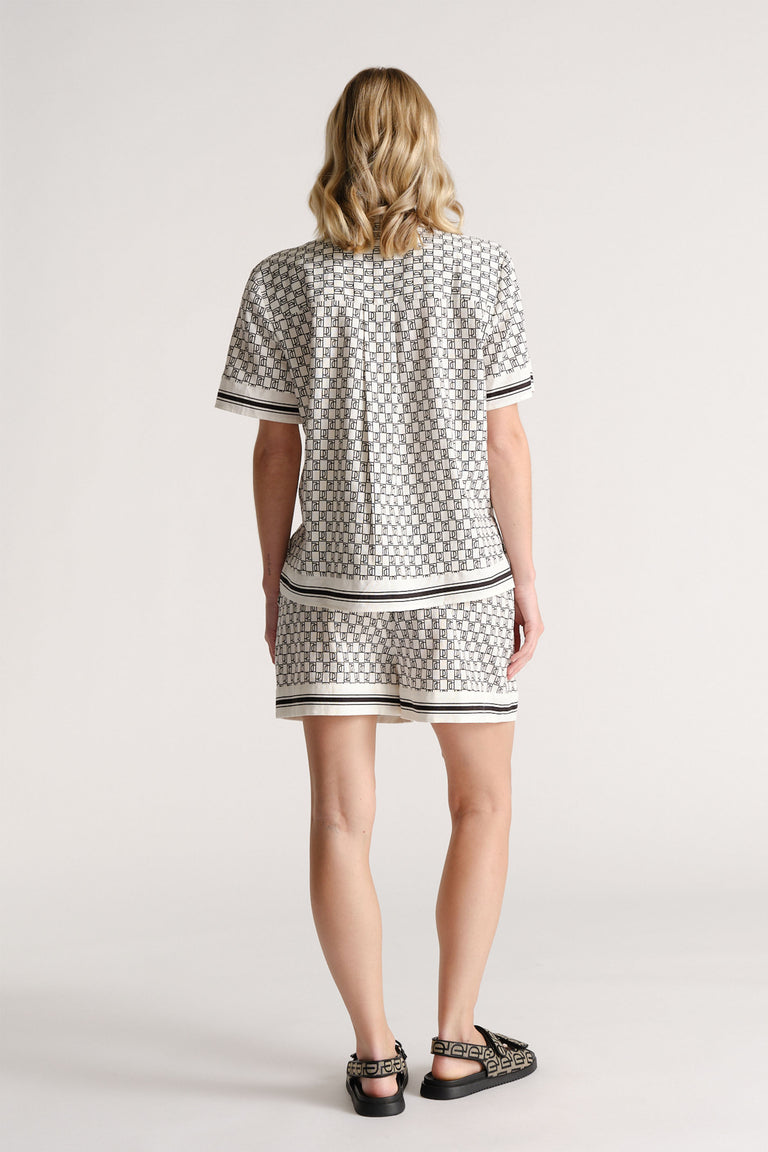 Woman wearing patterned short-sleeve top and matching shorts with striped trim, styled with patterned sandals, shown from behind.