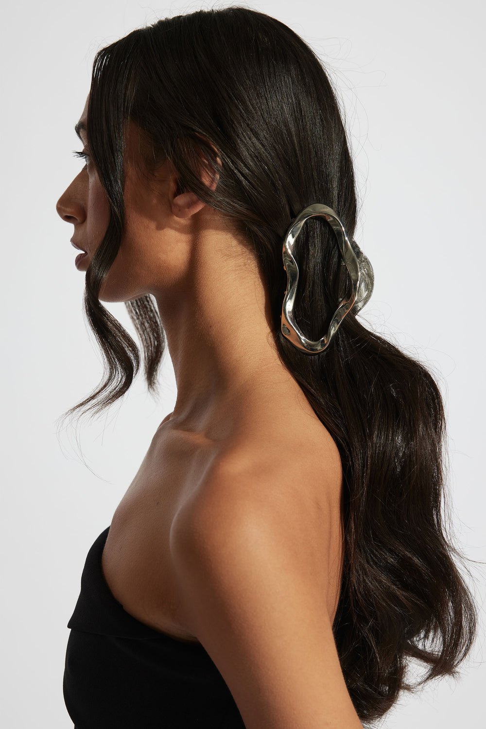 Side profile of woman with long dark hair secured by a silver wavy hair claw, wearing a black strapless top