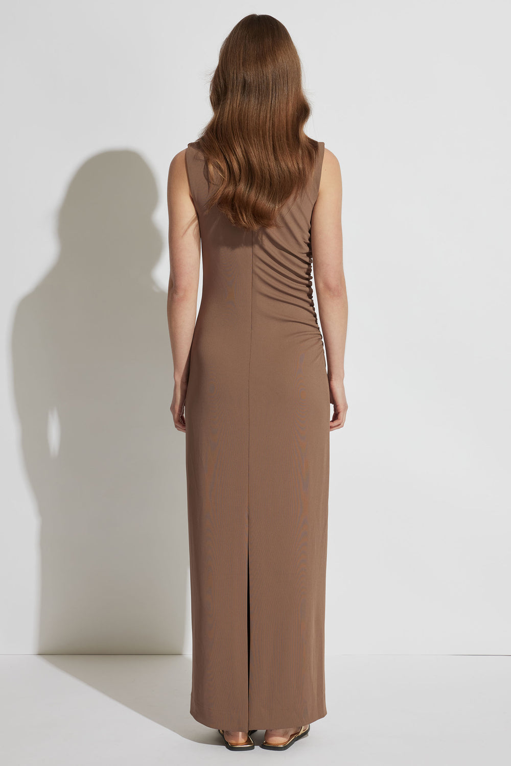 Woman wearing a sleeveless brown maxi dress with ruched side detail and a back slit, styled with flat sandals.