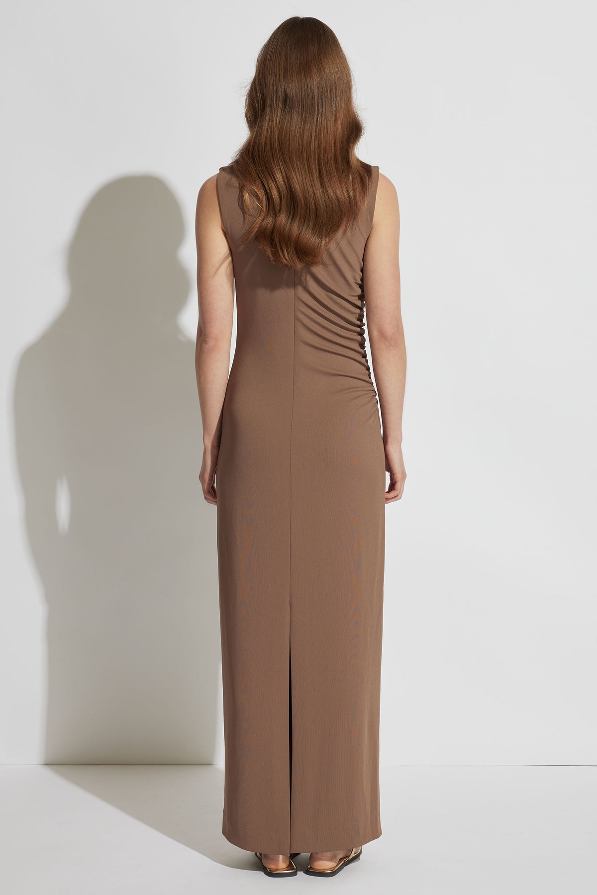 Woman wearing a sleeveless brown maxi dress with ruched side detail and a back slit, styled with flat sandals.