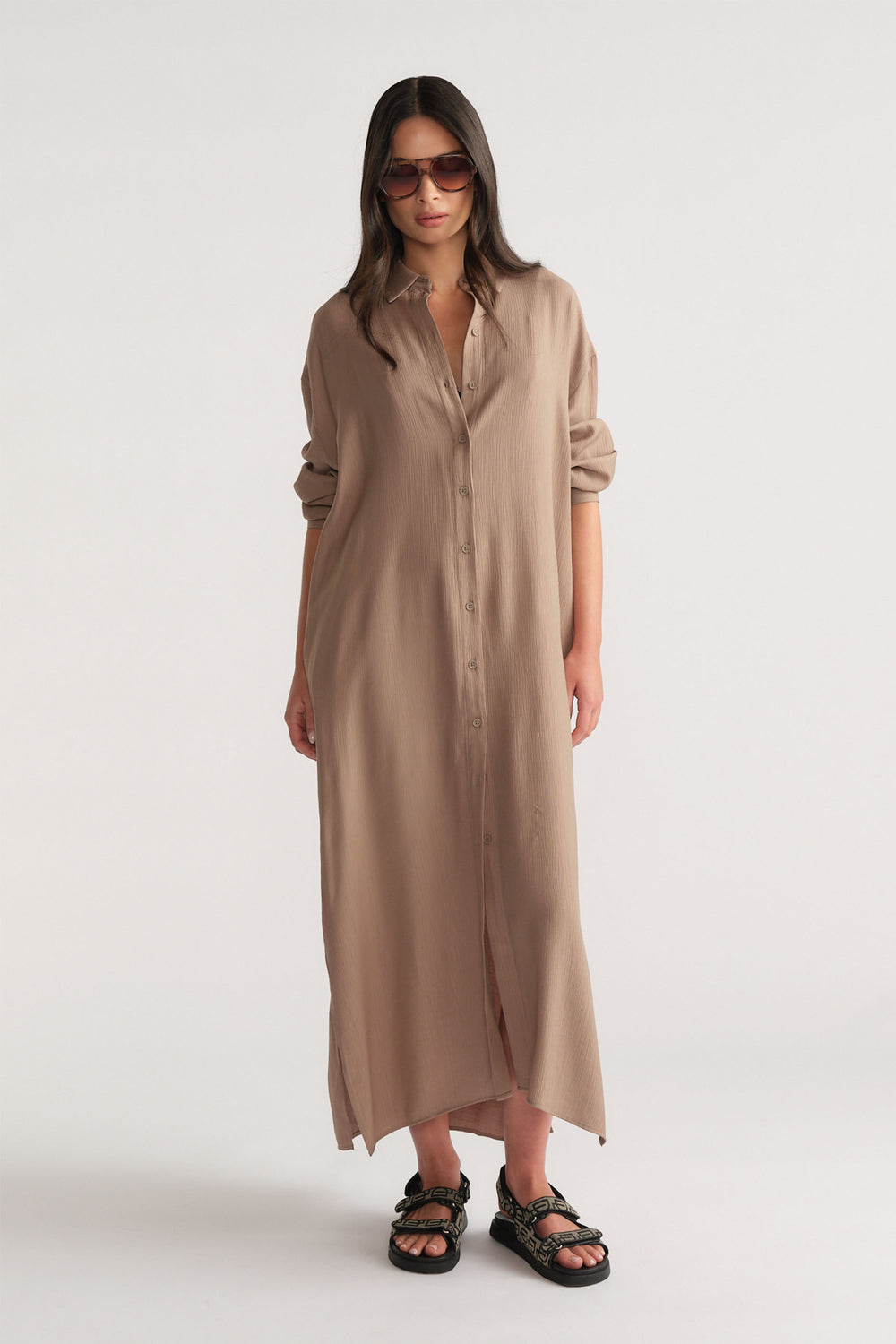 Woman wearing a relaxed fit barley-colored textured shirt dress with rolled sleeves and black sandals, styled with sunglasses