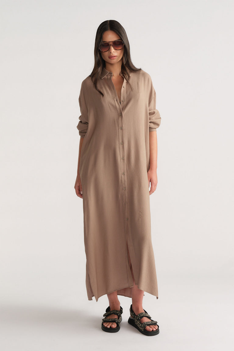 Woman wearing a relaxed fit barley-colored textured shirt dress with rolled sleeves and black sandals, styled with sunglasses