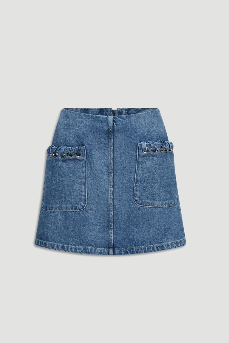 Blue denim skirt with front patch pockets featuring metal eyelet accents for a modern casual look.