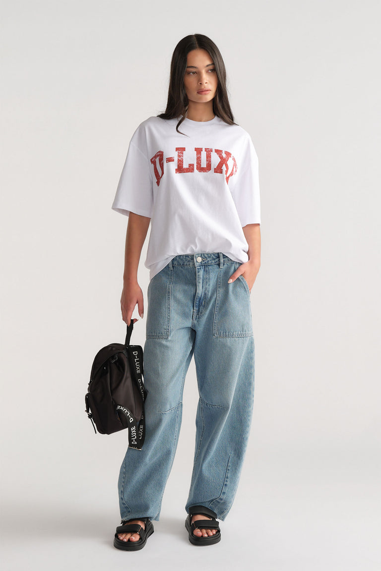 Woman wearing a white oversized distressed D-LUXE logo tee with drop shoulders, styled with relaxed blue jeans