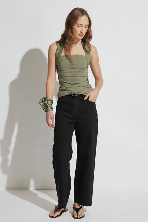 Woman wearing a fitted olive green ruched top paired with high-waisted black jeans and black sandals with a green wrist scarf