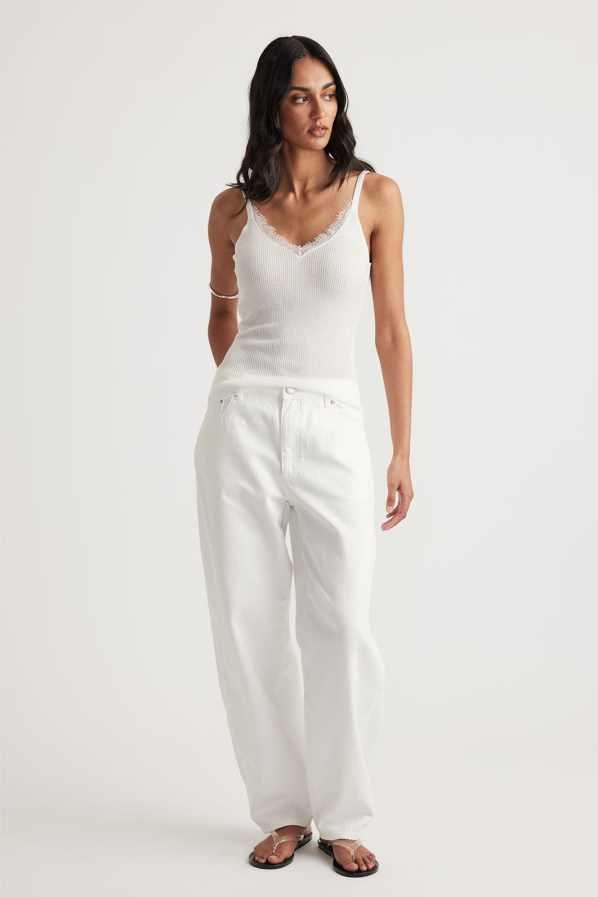 Woman wearing a fitted ivory lace-trimmed knit tank paired with loose white jeans and minimalist sandals