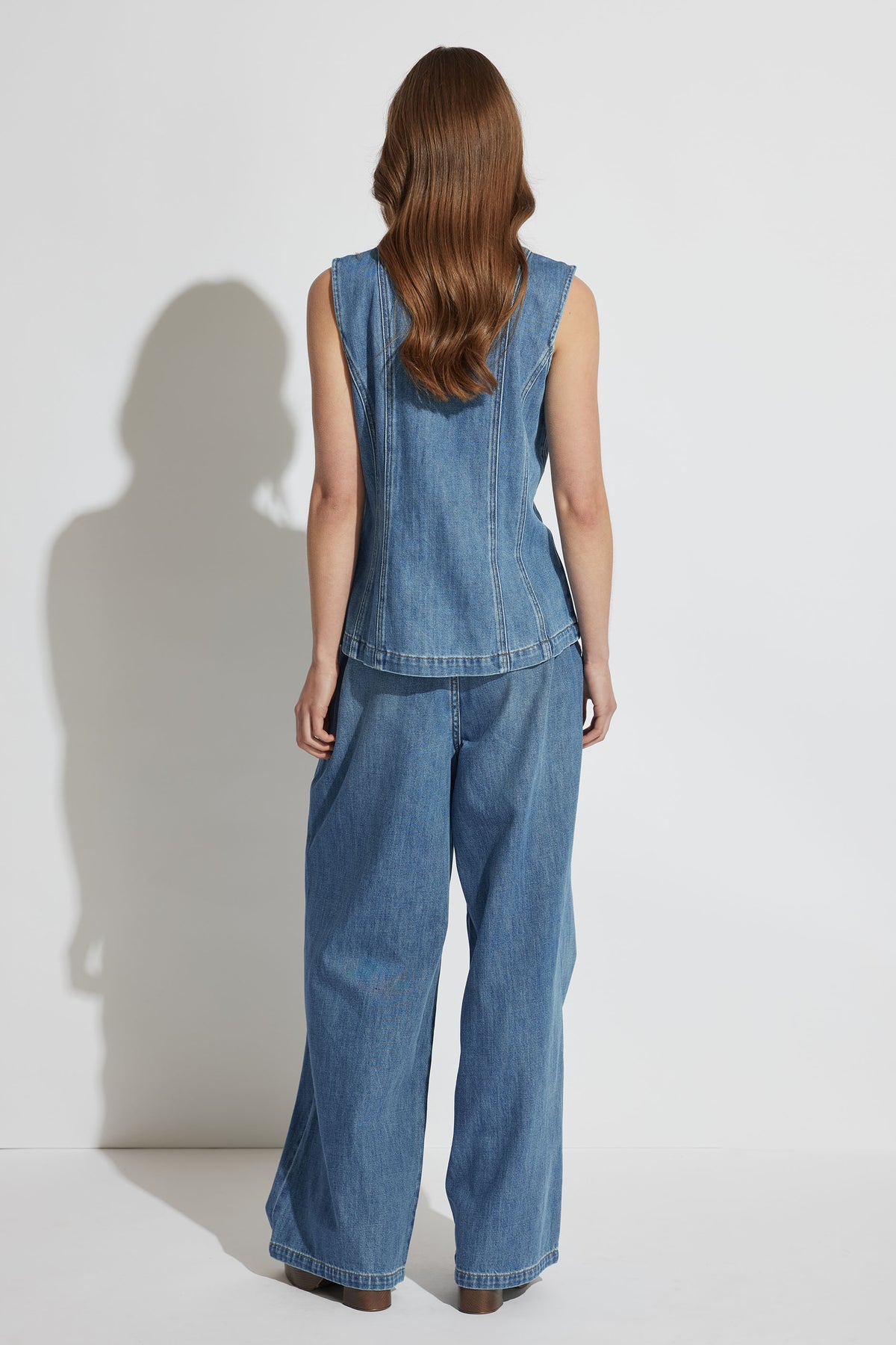 Woman wearing a sleeveless denim top paired with wide-leg pleated jeans in a relaxed, casual style from behind view.