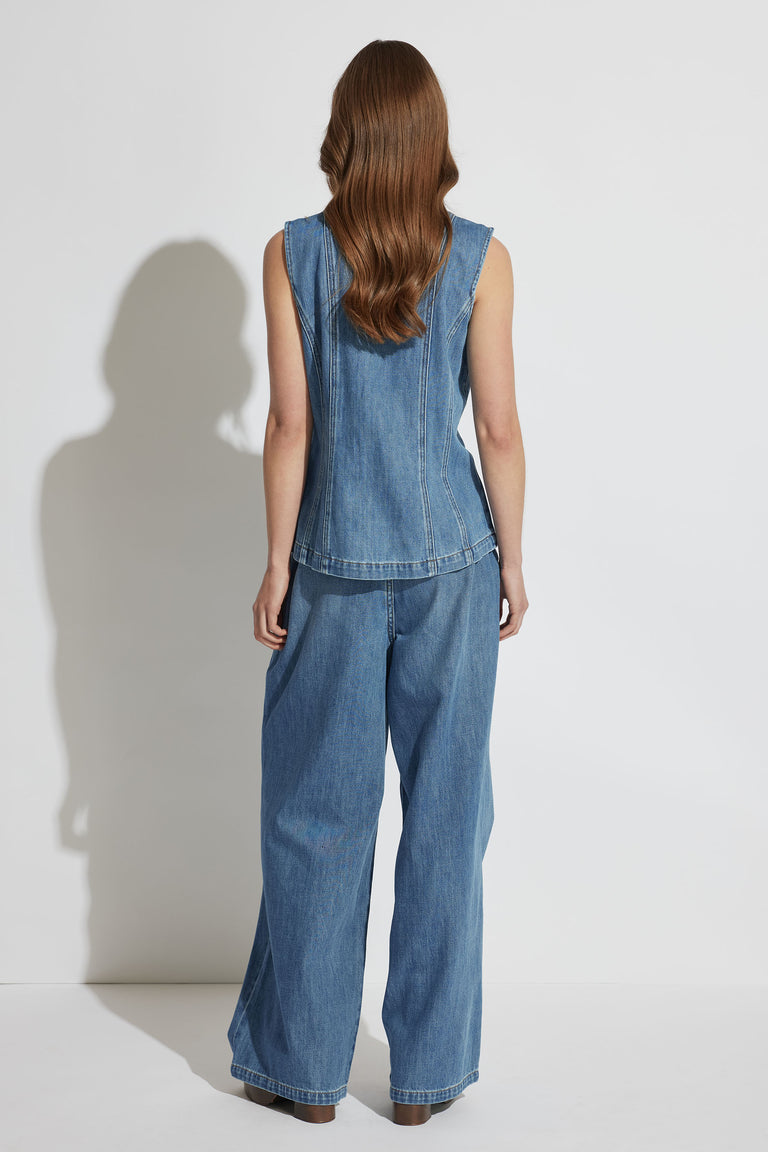 Woman wearing a sleeveless denim top paired with wide-leg pleated jeans in a relaxed, casual style from behind view.