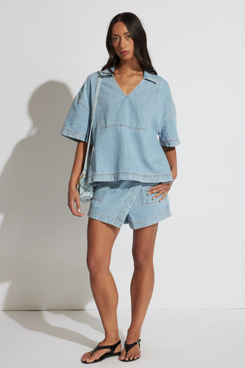 Woman wearing a light wash oversized denim shirt with matching high-waisted shorts and black sandals, posing front view.