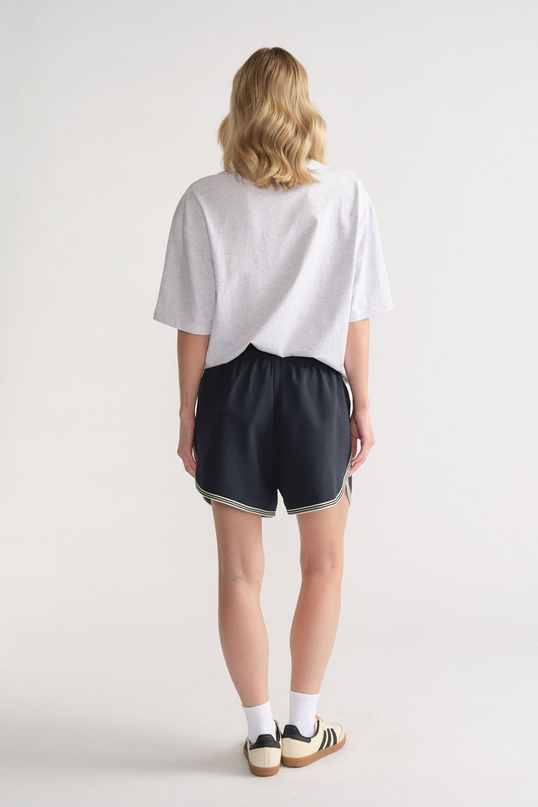 Back view of woman wearing relaxed black racer stripe shorts paired with a loose light grey tee and sneakers