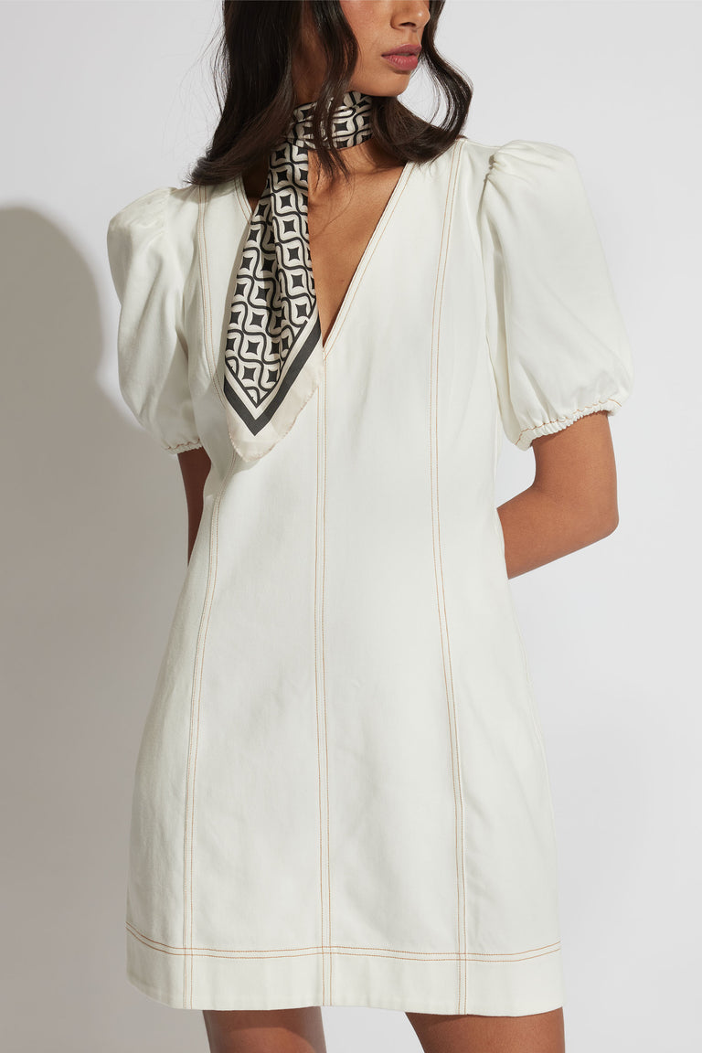 Woman wearing a white V-neck mini dress with puff sleeves, elasticated cuffs and contrast seam detailing