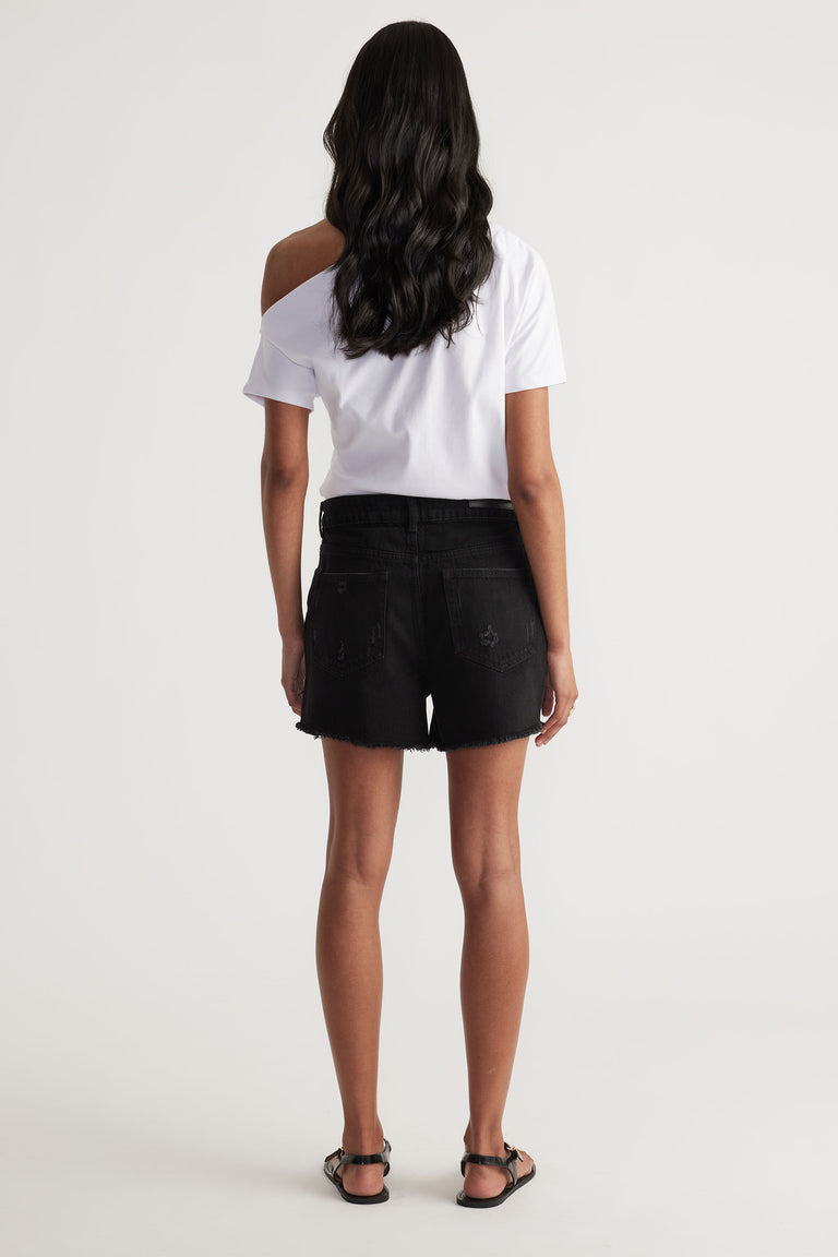Woman seen from behind wearing a white off-shoulder top paired with black distressed denim shorts and sandals
