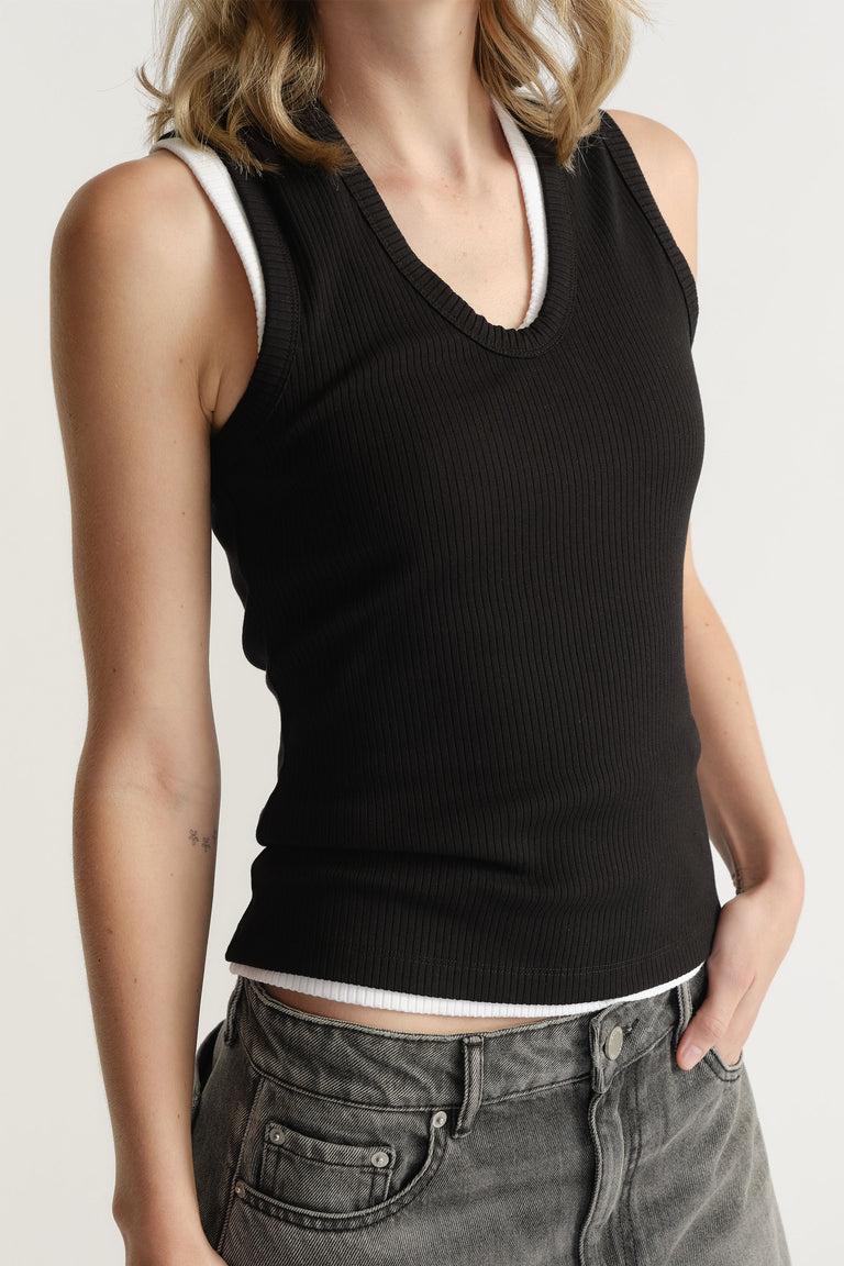 Woman wearing a fitted black ribbed tank layered over a white tank, paired with faded grey high-waisted jeans.
