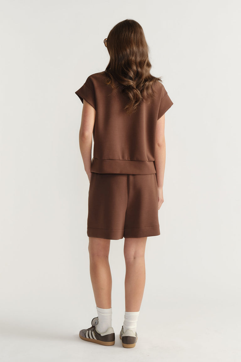 Back view of woman wearing relaxed brown neoprene shorts paired with a short-sleeve matching top and sneakers