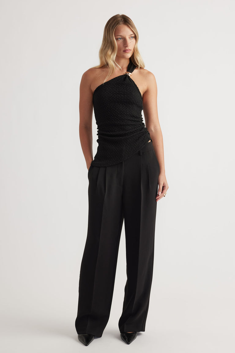 Woman wearing a textured black one-shoulder tank paired with high-waisted wide-leg black trousers and pointed heels