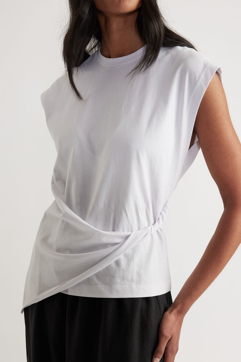 Woman wearing a white sleeveless top with twist detail at the waist paired with black wide-leg pants