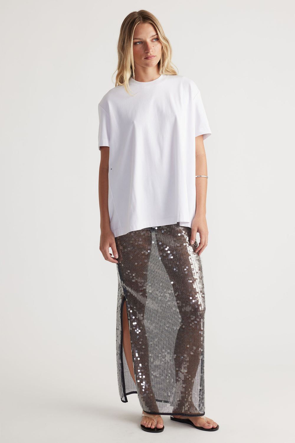 Woman wearing a white oversized tee and a semi sheer Savannah Sequin Skirt with side splits in portrait gallery position 1