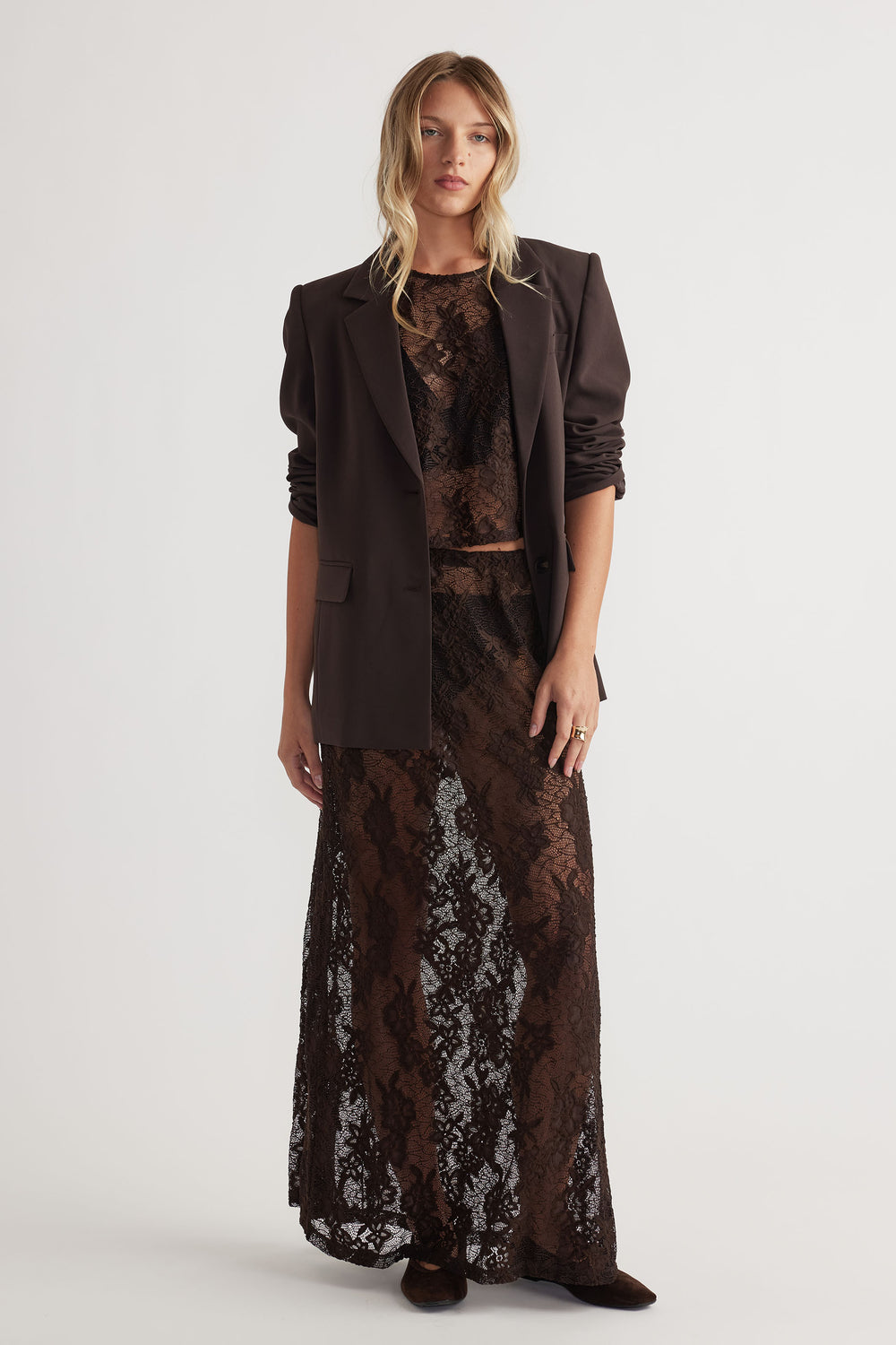 Woman styling a chocolate lace maxi skirt with a matching top and dark structured blazer for effortless elegance.
