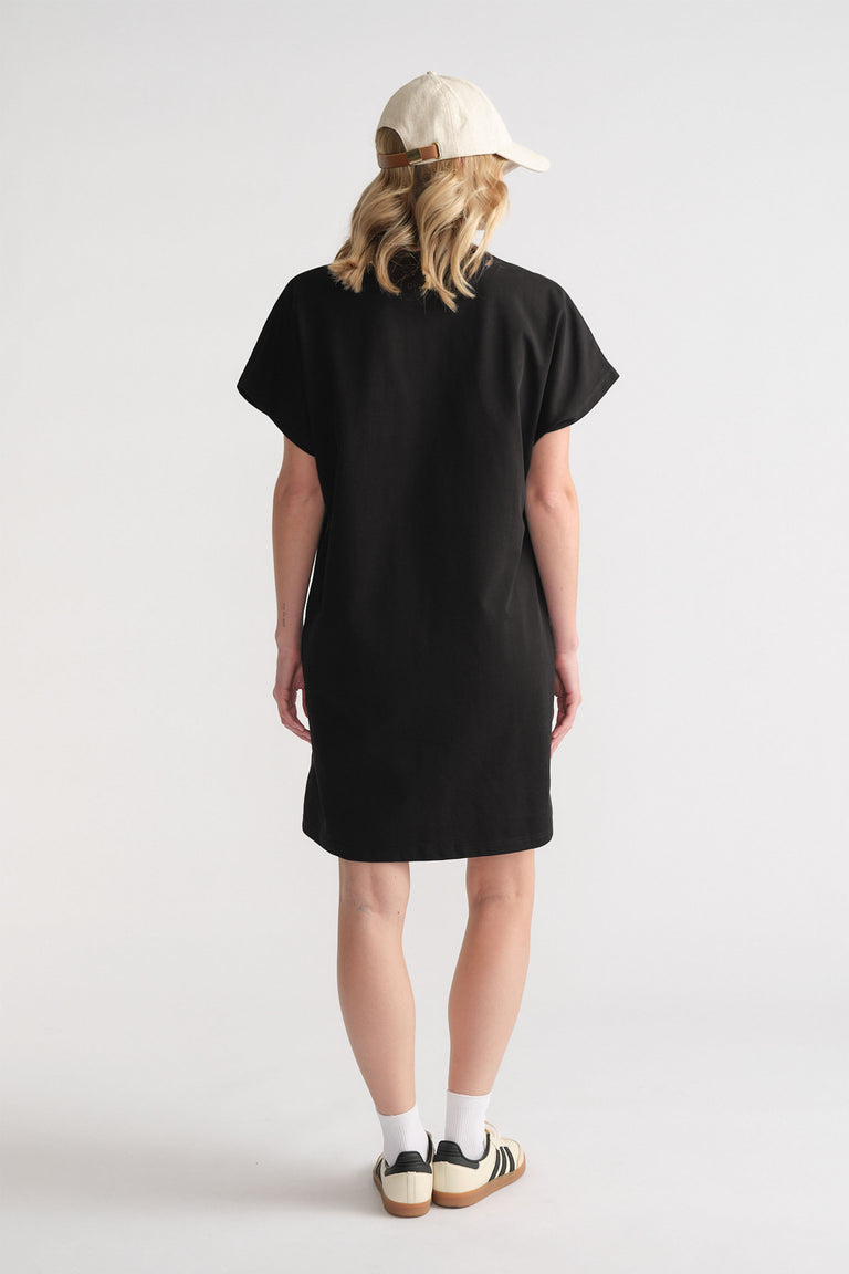 Back view of woman wearing a relaxed black short tee dress paired with white socks, sneakers, and a light beige cap