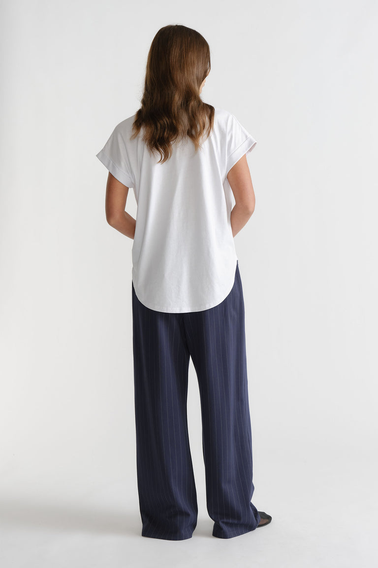 Woman wearing a white crew neck tee with short sleeves and a curved high low hem, viewed from behind