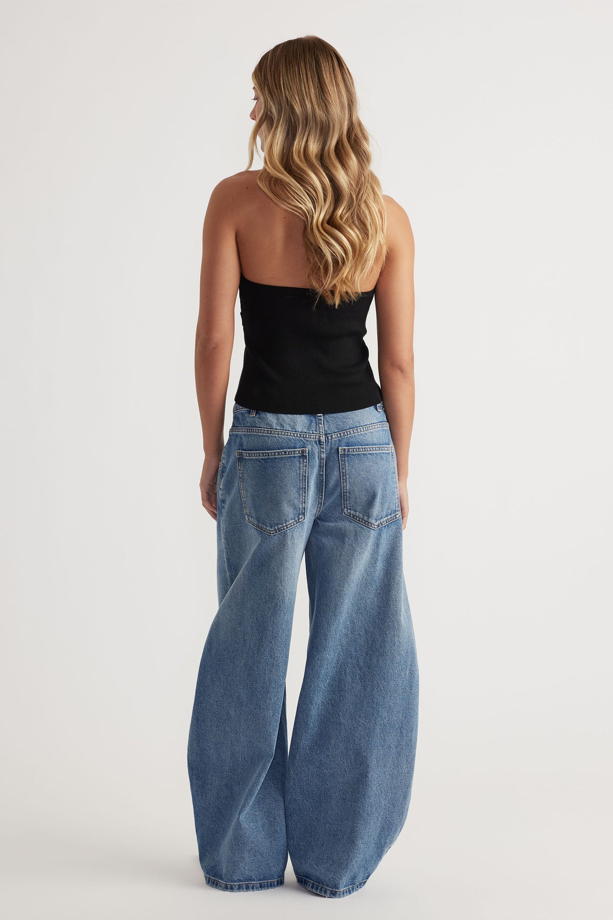 Back view of woman wearing a black halter tank paired with light blue wide-leg denim jeans for a relaxed look