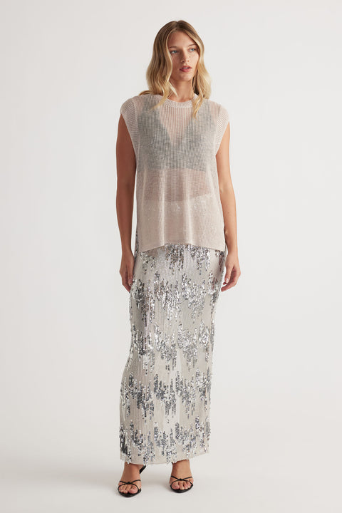 Woman wearing a soft beige knit tank layered over a black bralette, paired with a shimmering silver sequin maxi skirt
