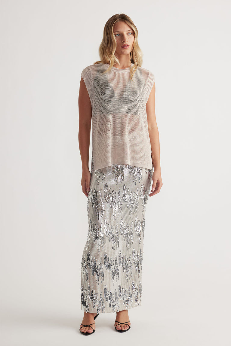 Woman wearing a soft beige knit tank layered over a black bralette, paired with a shimmering silver sequin maxi skirt