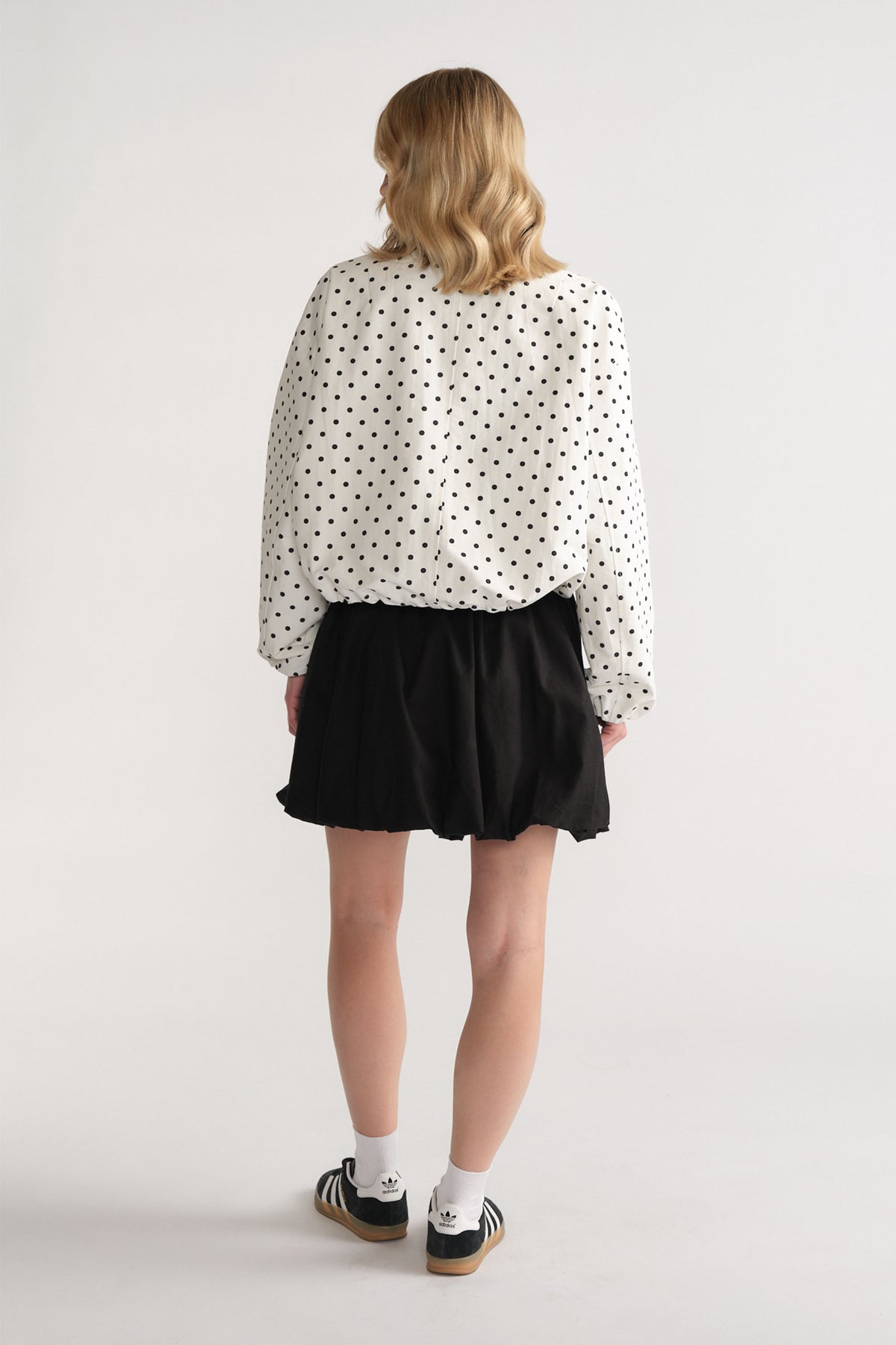 Back view of woman wearing a black bubble mini skirt paired with a loose white polka dot blouse and sneakers